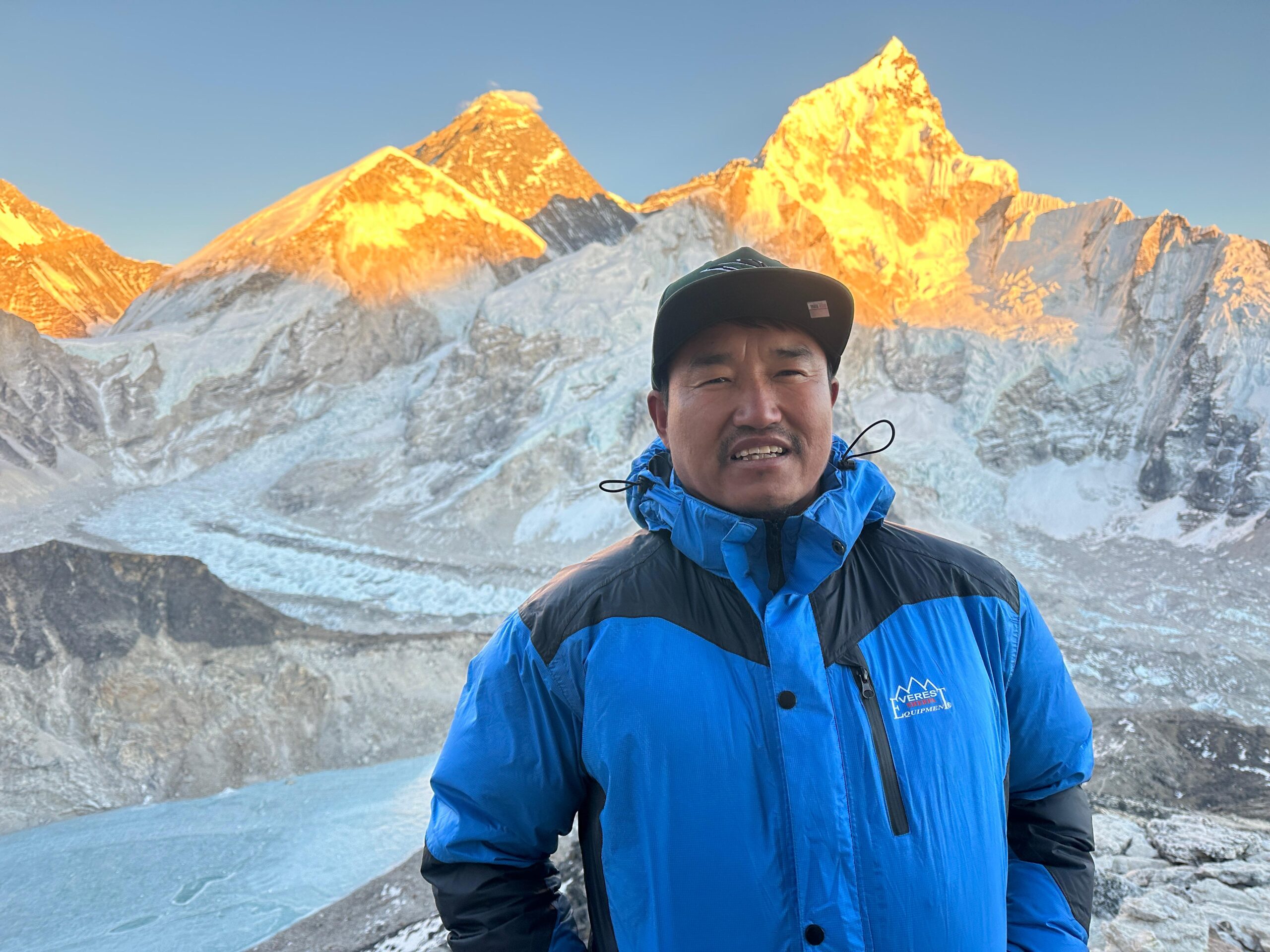 Our Story Lhomi man in blue jacket in front of golden peak mountains